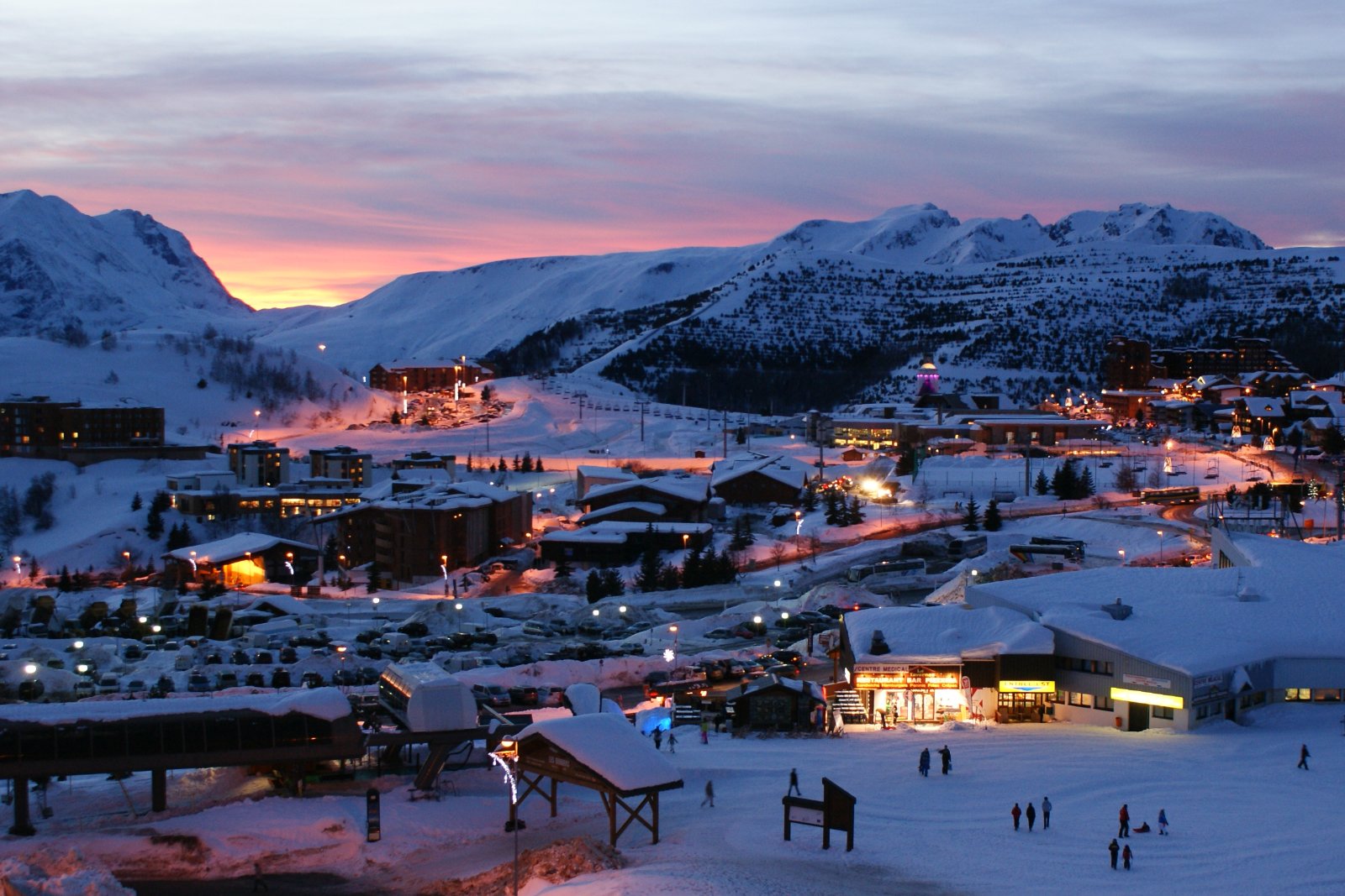 Photo : Kobzarius, CC BY 3.0, Wikimedia Commons La station de l'Alpe d'Huez illuminée à la tombée du jour, au pied des pistes